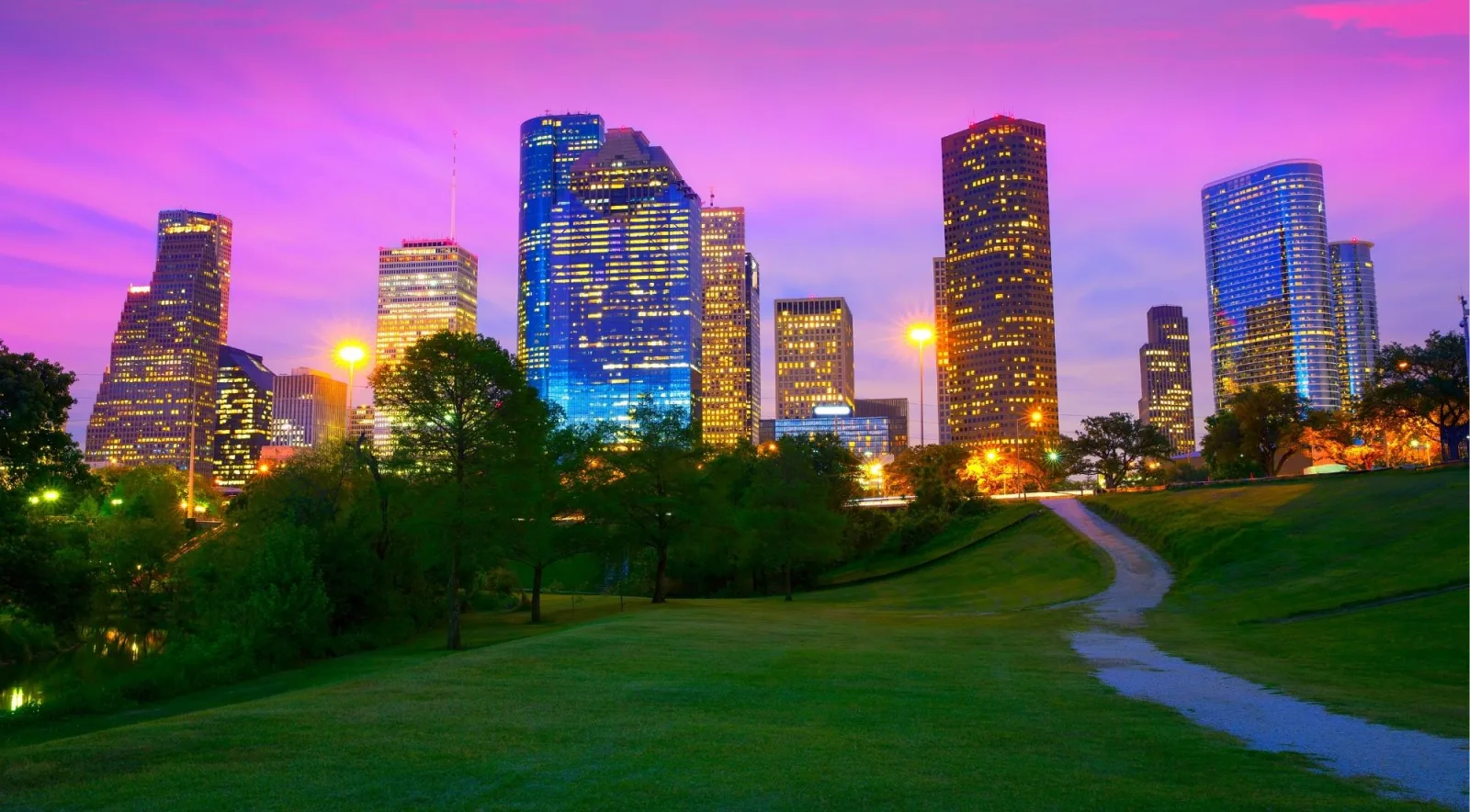 The Houston skyline under a purple sunset sky above a green park