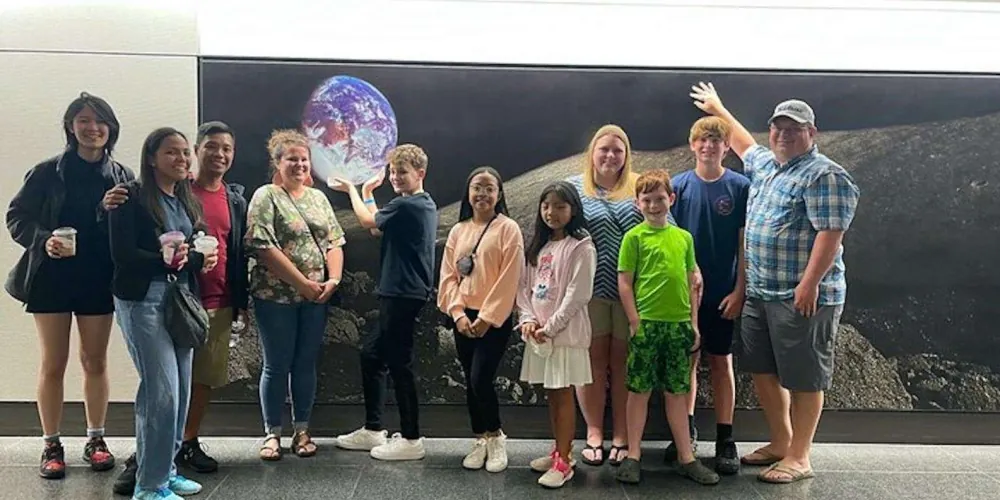 Visitors holding an illuminated Earth globe beside a lunar-surface photo wall at Space Center Houston